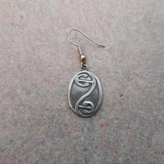 Silver metal oval earring with design found in the Manor Library by newspaper table.